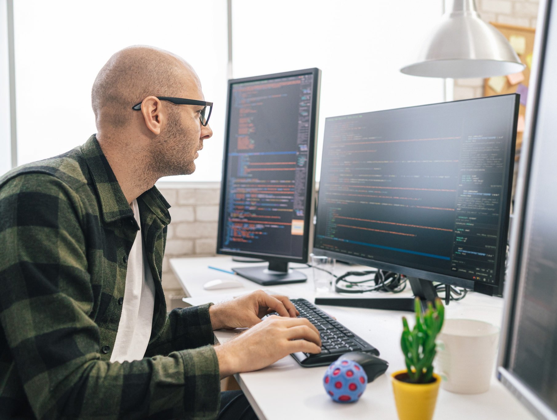 A man wearing glasses is coding on a computer.
